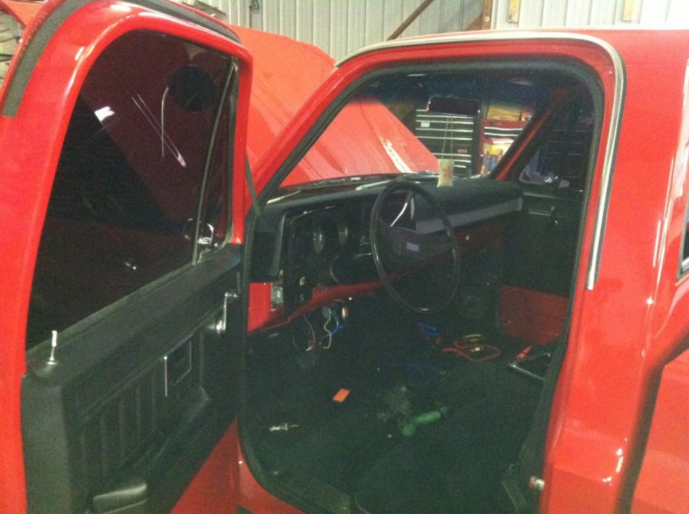 Red vintage truck with the door open to display the interior. A new stereo system is being installed.