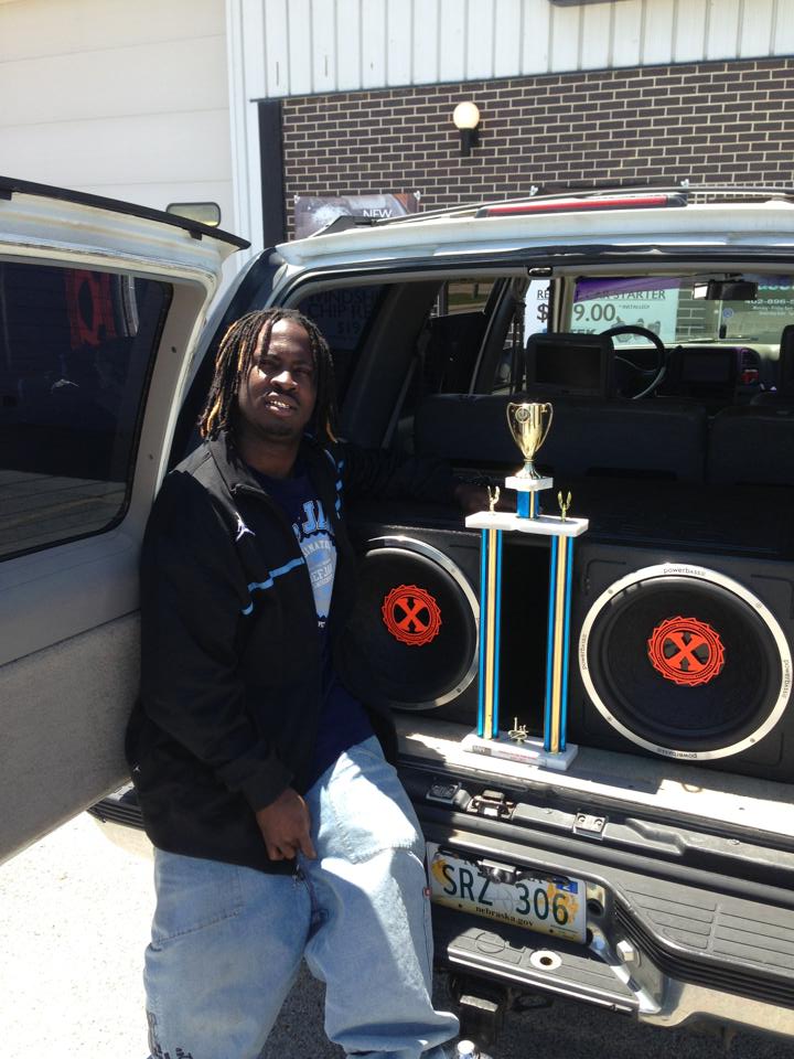 A man posing with a trophy and a speaker system in the back of his car