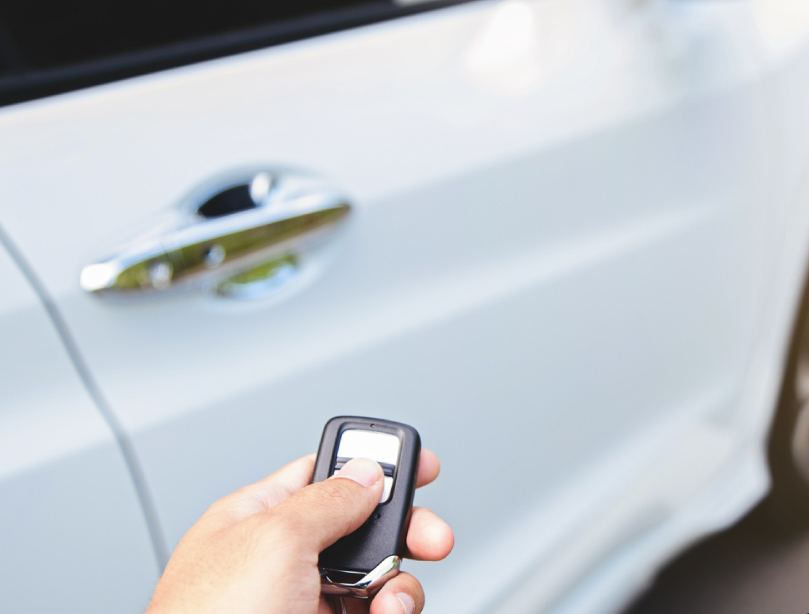 A hand holding a remote car starter with a white car in the background